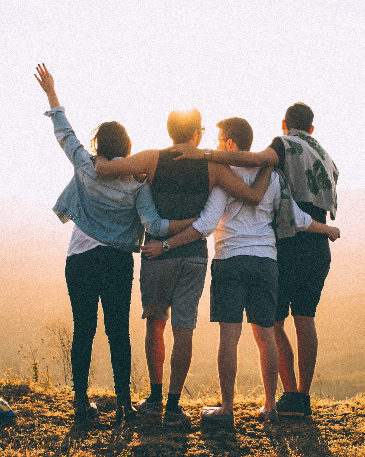 Four guests arm in arm at golden hour, looking out over open country