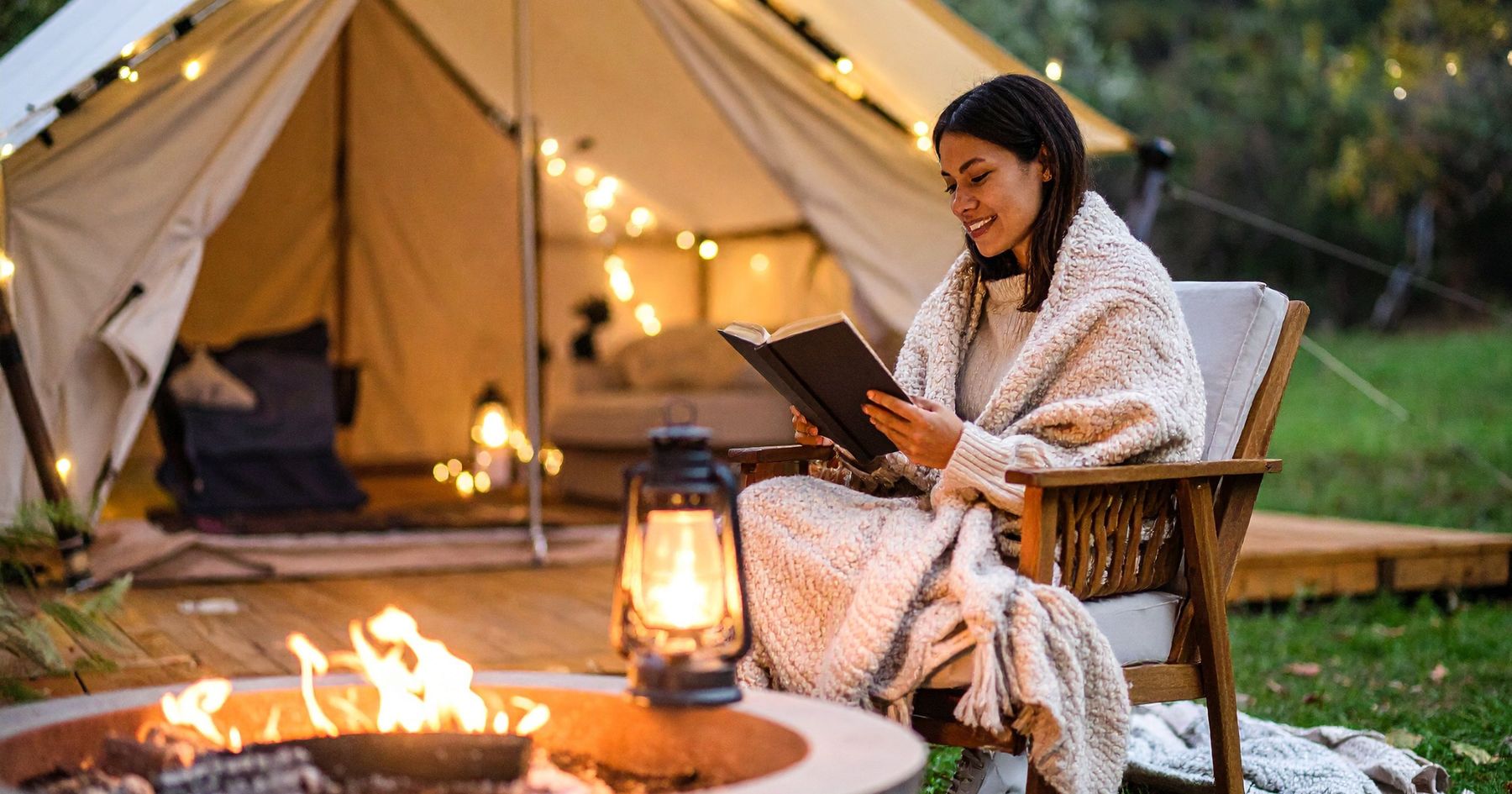 A glamping tent lit at dusk beside a fire pit
