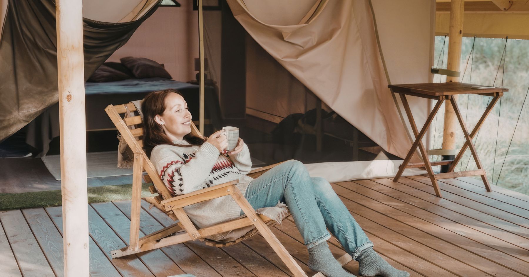 A guest with coffee on the deck of an Out&West canvas tent
